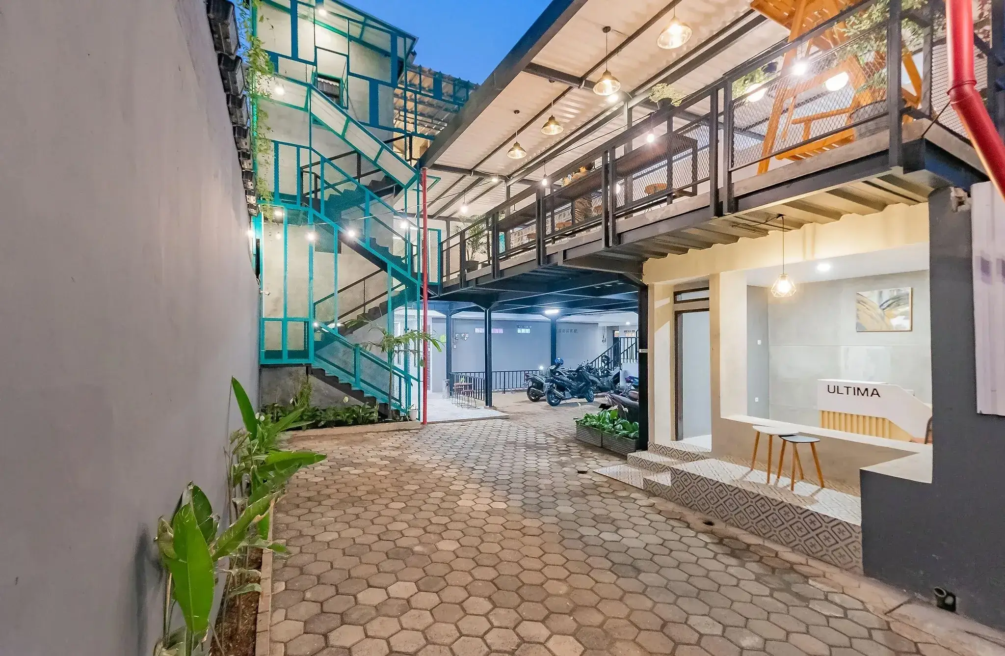 Courtyard of Ultima Guest House at dusk with its teal steel staircase and warm lights